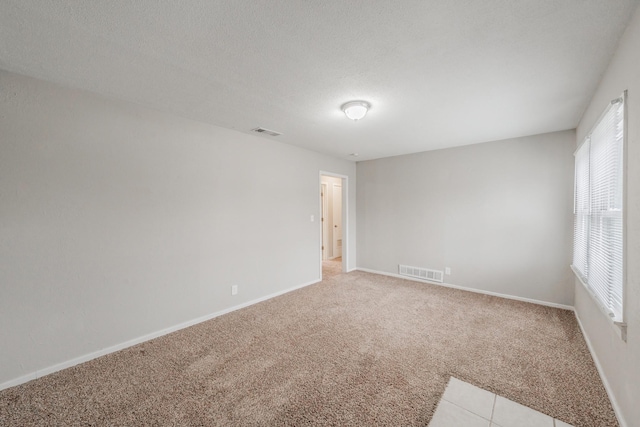 unfurnished room featuring light carpet, a textured ceiling, visible vents, and baseboards