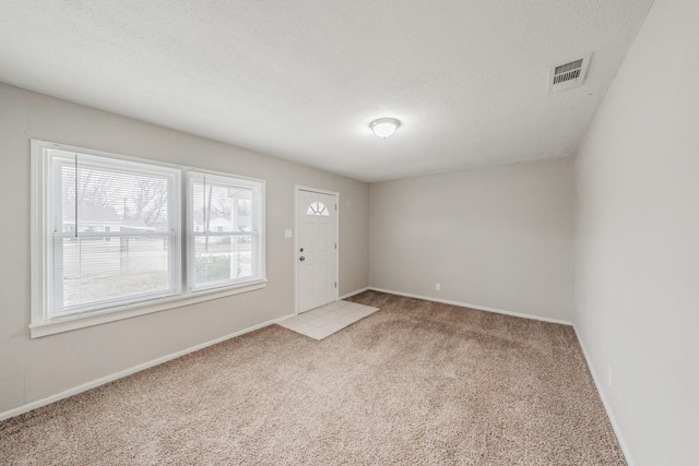 carpeted entrance foyer featuring visible vents, baseboards, and a textured ceiling