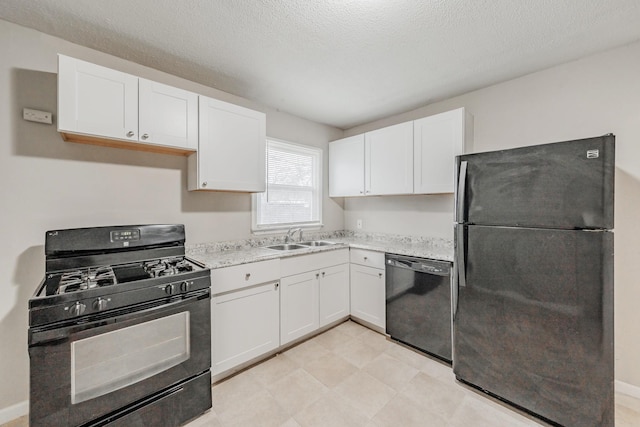 kitchen with a textured ceiling, light stone counters, a sink, white cabinetry, and black appliances