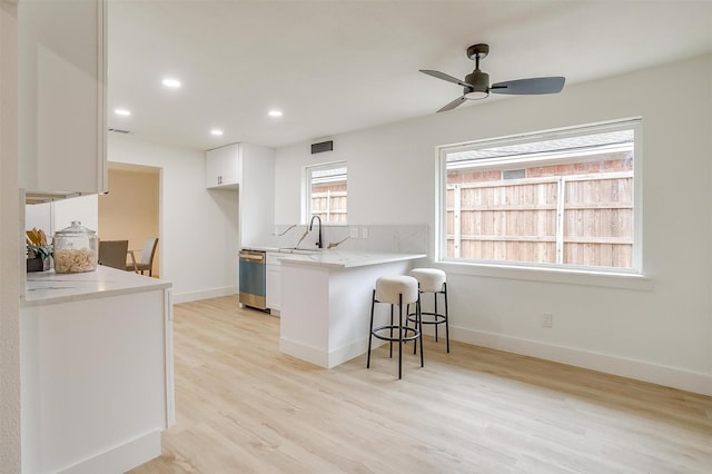 kitchen featuring light countertops, white cabinets, a sink, dishwasher, and a peninsula