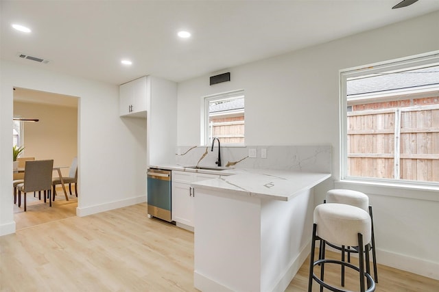 kitchen with visible vents, white cabinets, light stone counters, stainless steel dishwasher, and a sink