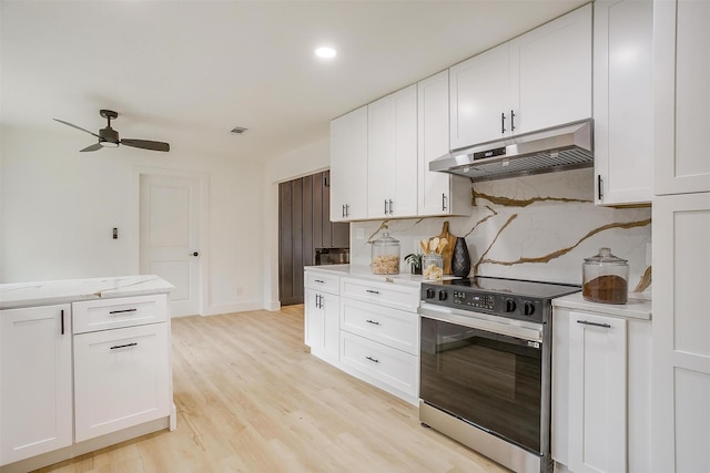 kitchen with electric stove, light stone counters, under cabinet range hood, white cabinetry, and backsplash