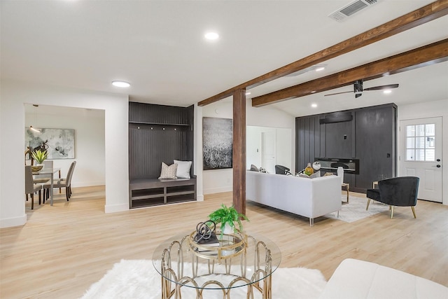 living room with beam ceiling, light wood-type flooring, visible vents, and baseboards