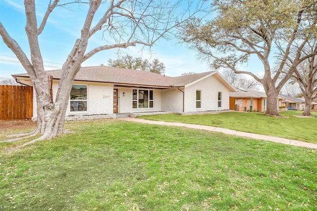 single story home featuring brick siding, a front lawn, a shingled roof, and fence