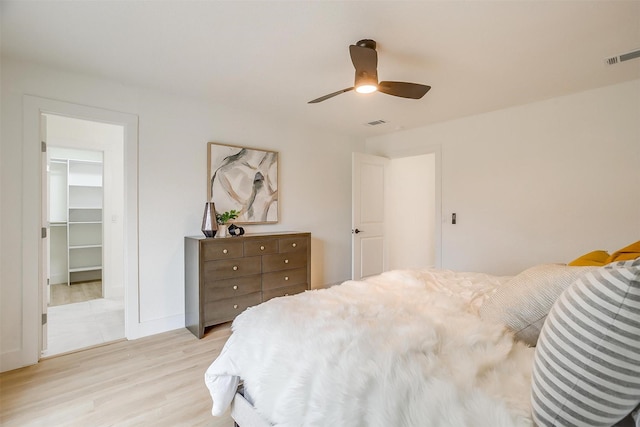 bedroom featuring ceiling fan, visible vents, light wood-style floors, a closet, and a walk in closet