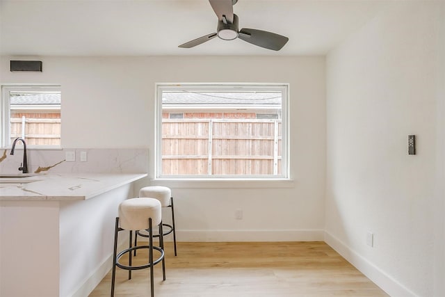 kitchen with baseboards, a ceiling fan, light wood-style flooring, a kitchen bar, and a sink