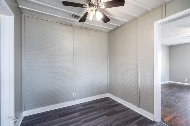 spare room with a ceiling fan, baseboards, dark wood finished floors, and brick wall