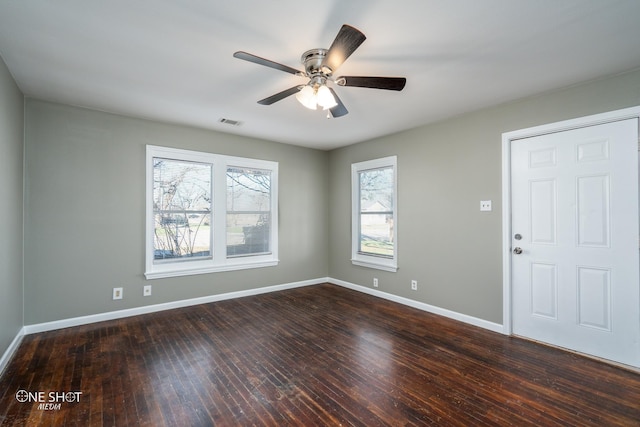 empty room featuring a ceiling fan, visible vents, dark wood finished floors, and baseboards