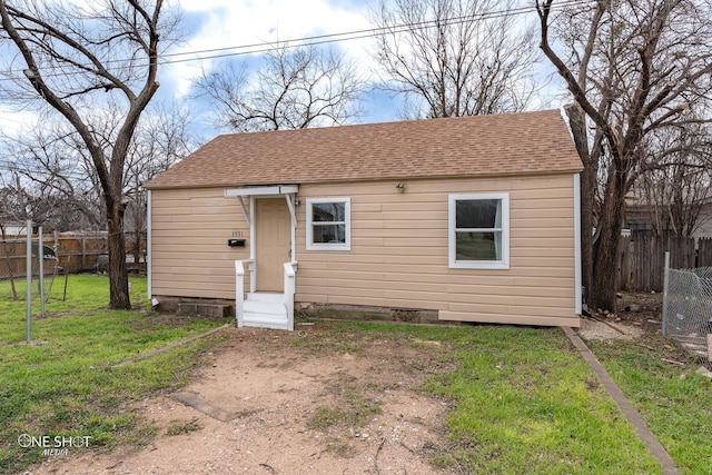 exterior space with a front yard, roof with shingles, and fence