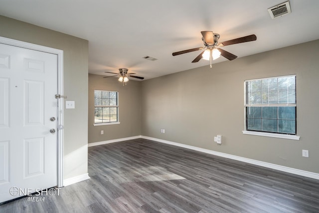 empty room featuring dark wood-style floors, ceiling fan, visible vents, and baseboards