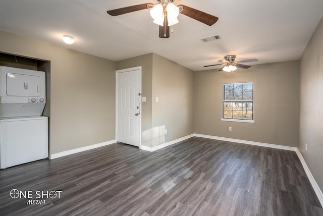 empty room featuring baseboards, visible vents, dark wood finished floors, and stacked washer / drying machine