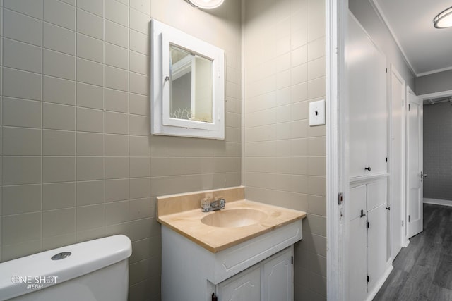 half bathroom featuring toilet, wood finished floors, tile walls, and vanity