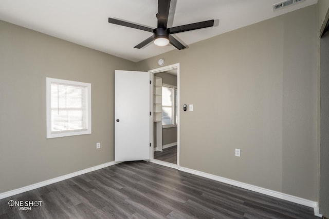 empty room featuring a ceiling fan, visible vents, dark wood finished floors, and baseboards