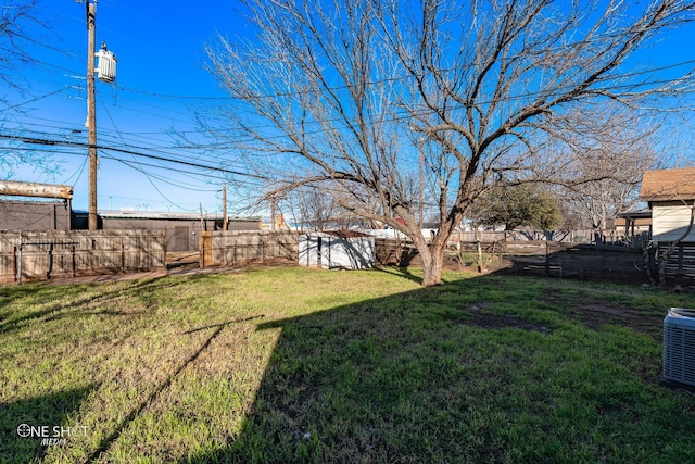 view of yard with a fenced backyard, central AC, and a storage shed