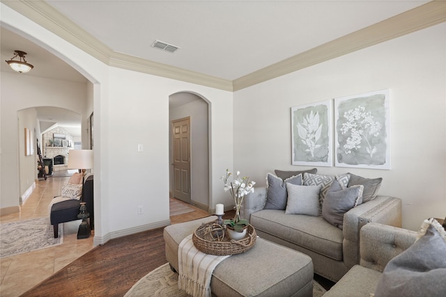 living area with baseboards, visible vents, arched walkways, wood finished floors, and crown molding