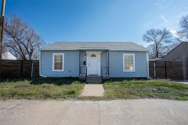 bungalow-style home with roof with shingles and fence