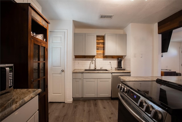 kitchen with light stone counters, stainless steel appliances, visible vents, a sink, and light wood-type flooring