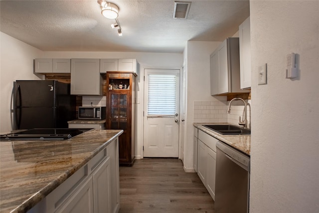 kitchen with stone countertops, visible vents, dark wood-style floors, black appliances, and a sink