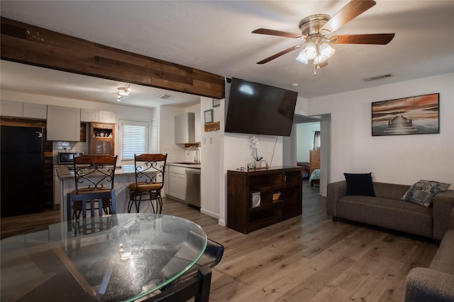 living area with ceiling fan, beamed ceiling, wood finished floors, and visible vents