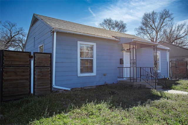 view of front facade featuring a shingled roof and fence