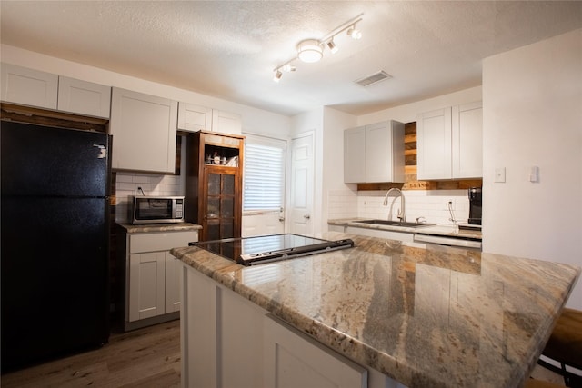 kitchen with stainless steel microwave, visible vents, freestanding refrigerator, a sink, and light stone countertops