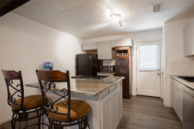 kitchen featuring dark wood-style floors, visible vents, backsplash, light stone countertops, and black appliances