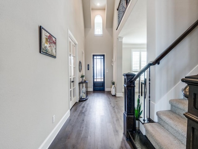 entryway featuring baseboards, dark wood-type flooring, a towering ceiling, and stairs