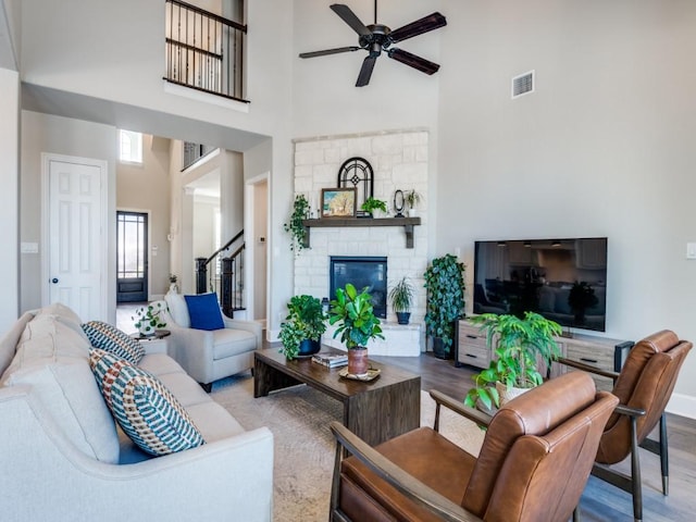 living room with ceiling fan, visible vents, wood finished floors, and a towering ceiling