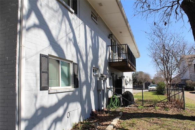 view of property exterior featuring brick siding, fence, and a balcony