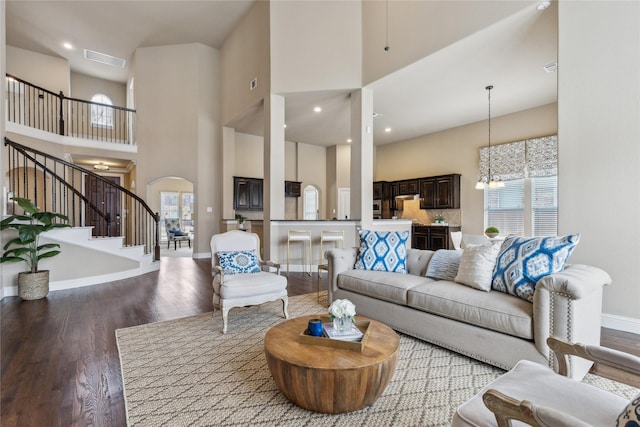 living area with arched walkways, a chandelier, wood finished floors, visible vents, and stairs