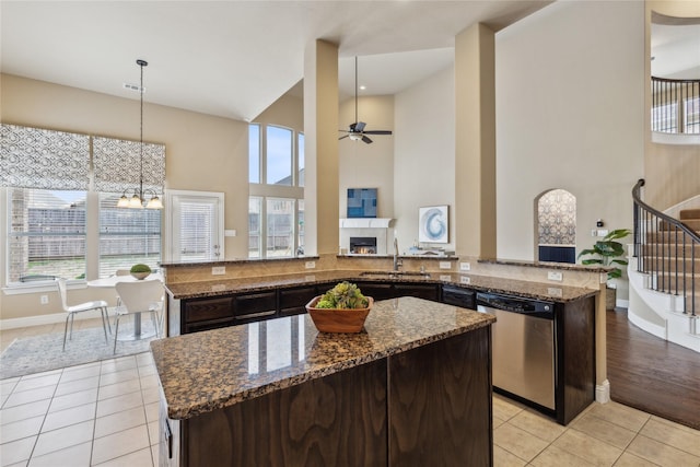 kitchen featuring stainless steel dishwasher, light tile patterned flooring, a sink, dark stone counters, and a lit fireplace