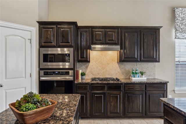 kitchen with dark stone counters, stainless steel appliances, backsplash, and under cabinet range hood