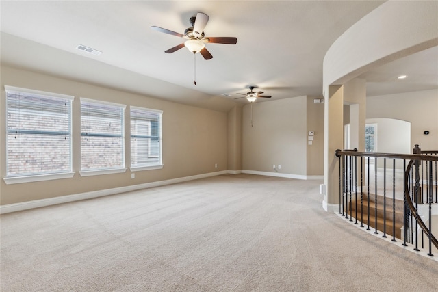 empty room with light colored carpet, visible vents, arched walkways, and baseboards