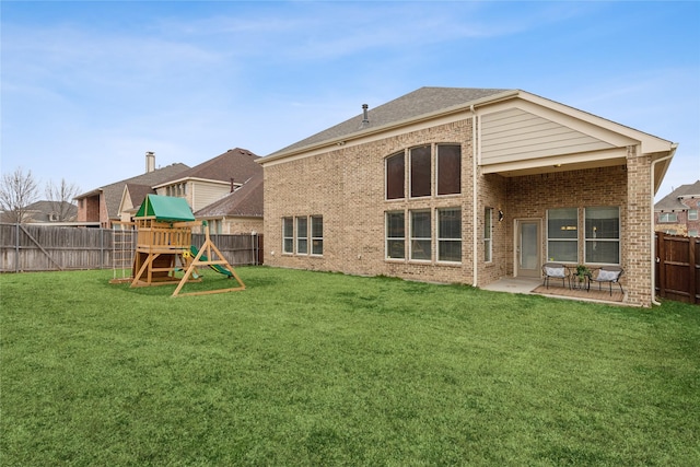 rear view of property with a fenced backyard, a yard, a patio area, a playground, and brick siding