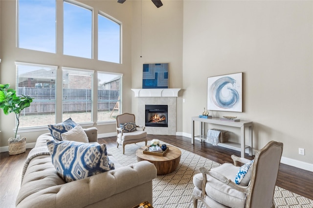 living area featuring a high end fireplace, a towering ceiling, baseboards, and wood finished floors