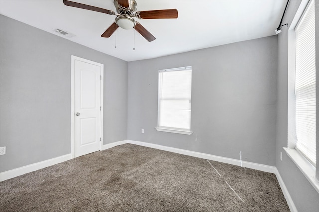 carpeted spare room featuring ceiling fan, plenty of natural light, visible vents, and baseboards