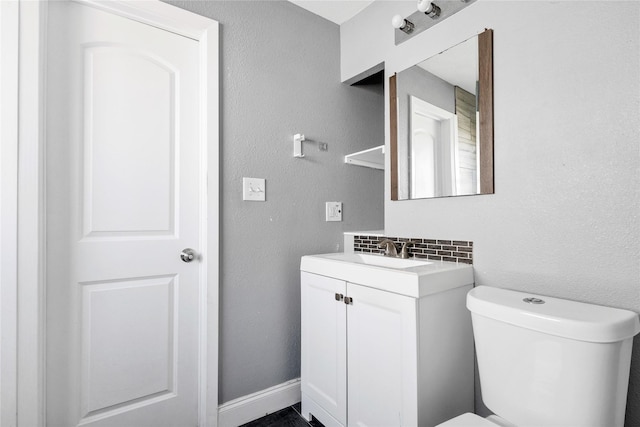 half bathroom featuring baseboards, decorative backsplash, a textured wall, toilet, and vanity