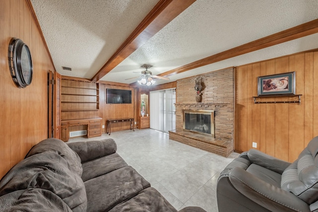 living area with a textured ceiling, wooden walls, a fireplace, visible vents, and beamed ceiling