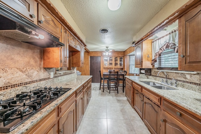 kitchen featuring visible vents, brown cabinets, black gas cooktop, under cabinet range hood, and a sink