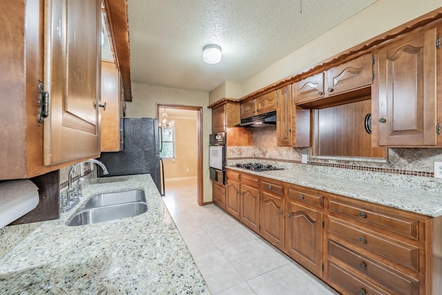 kitchen with brown cabinets, light stone countertops, under cabinet range hood, gas stovetop, and a sink