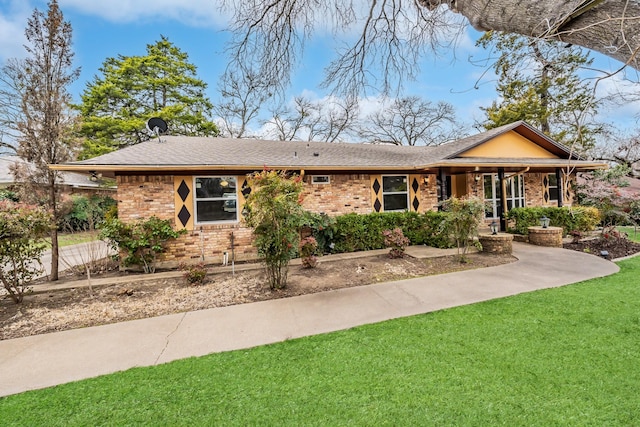 ranch-style home with a shingled roof, a front lawn, and brick siding