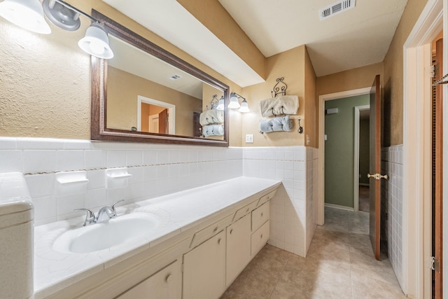 bathroom featuring visible vents, wainscoting, tile patterned floors, vanity, and tile walls