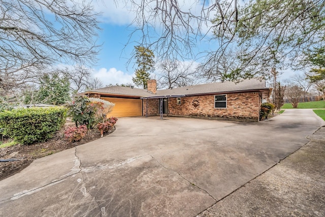 view of front of house with driveway, an attached garage, a chimney, and brick siding