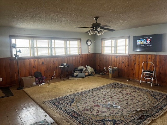 interior space featuring a textured ceiling, ceiling fan, wood walls, and wainscoting