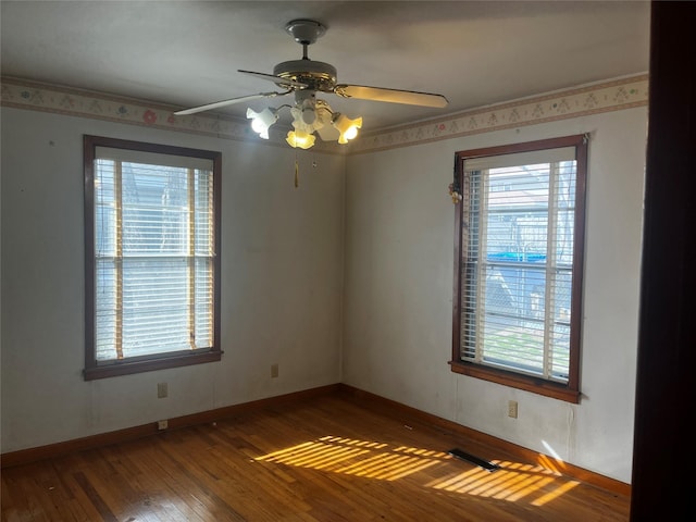 unfurnished room with a ceiling fan, wood-type flooring, visible vents, and baseboards