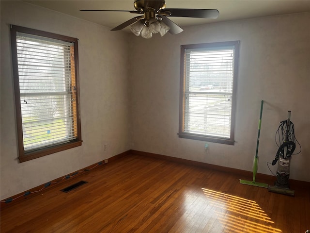 empty room featuring plenty of natural light, wood finished floors, visible vents, and baseboards