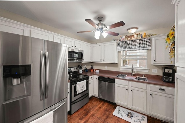 kitchen with stainless steel appliances, a sink, white cabinetry, dark wood-style floors, and dark countertops