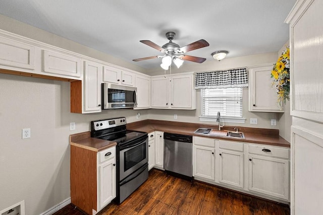 kitchen featuring stainless steel appliances, dark countertops, a sink, and white cabinetry