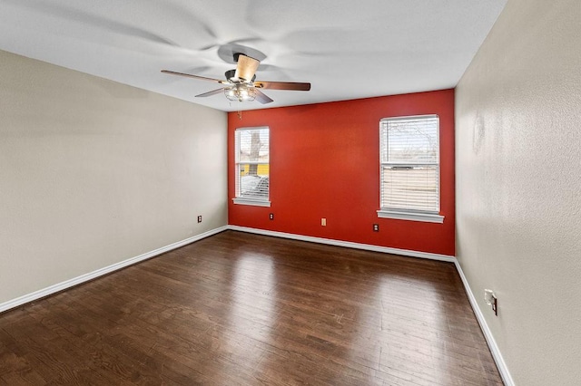 empty room with dark wood-style flooring, a ceiling fan, and baseboards