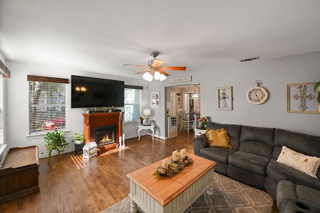 living room with dark wood-type flooring, visible vents, baseboards, a ceiling fan, and a glass covered fireplace